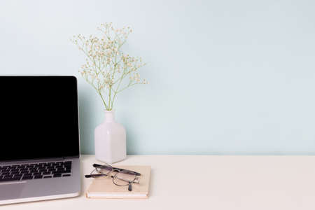 Feminine workspace with laptop, flowers and office supply in front of blue background. Online work, e-learning concept with copy space.の写真素材