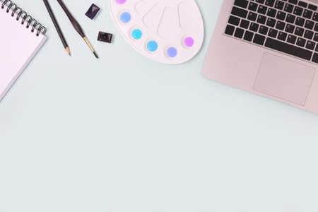 Top view of tools for painting on a blue pastel background. Laptop, watercolor, paintbrush and stationery.の写真素材
