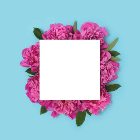 Square paper card mockup on a blue background. Frame made of pink peony flowers with copyspace.の写真素材