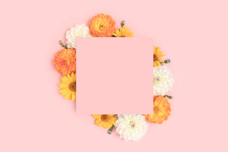 Blank paper card mockup with border frame made of dahlia flowers on a pink pastel background. Floral...