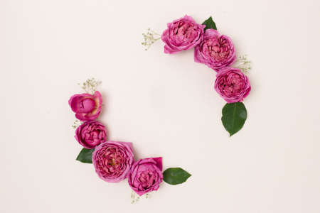 Round frame made of rose and green leaves on a beige background. Flower wreath. Festive concept.の写真素材