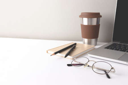 Workspace with laptop, glasses, stationery and cup of coffee in front of gray background.