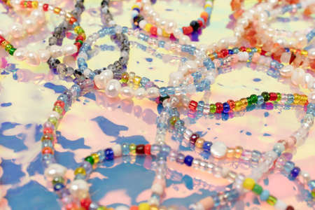 Closeup of necklaces and bracelets made from colorful beads and pearls on a pink holographic background.の写真素材