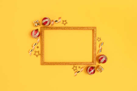 Glittering frame made of red Christmas balls and gold confetti on a yellow background. Bright festive concept with copy space.の写真素材