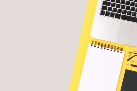 Layout of stationery and laptop on a gray and yellow background. Neat workspace with open empty notepad.の写真素材