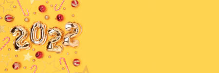 Banner with 2022 inflatable golden balloons and Christmas decorations on a yellow background. New Year's concept with copyspace.の写真素材