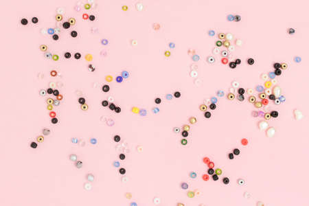 Composition with colorful beads scattered on a pink pastel background.