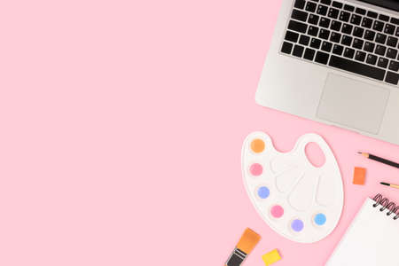 Tools for painting on a pink pastel background. Laptop, watercolor, paintbrush and stationery. Workspace for online education with copyspace.の写真素材