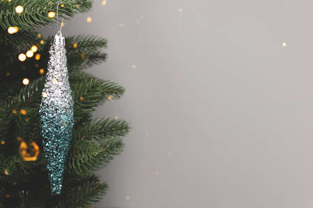 Shiny blue Christmas icicle hanging on a fir branch. New Year decoration in front of gray background with place for text.の写真素材
