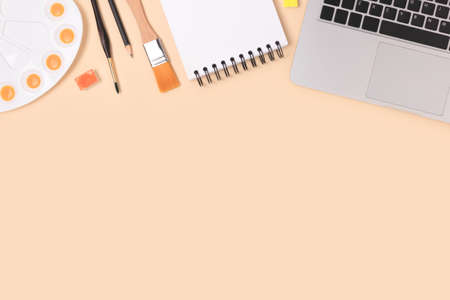 Tools for painting on a beige background. Laptop, watercolor palette, paintbrush and stationery. Workspace for homeschooling with copyspace.の写真素材