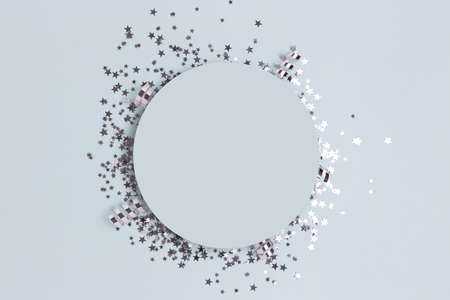 Round frame made of silver colored confetti on a blue pastel background.の写真素材