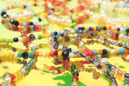 Closeup of necklaces and bracelets made from colorful beads and pearls on a yellow holographic...