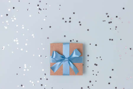 Gift box with tied ribbon and silver stars confetti with copy space on a blue background.の写真素材