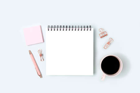 Workspace with square notepad mockup, pink stationery and coffee cup on a blue background. Education concept.の写真素材