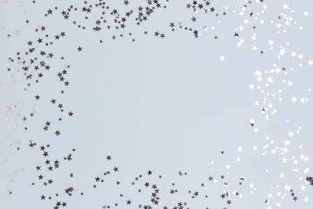 Border frame made of silver colored stars confetti on a blue pastel background.の写真素材