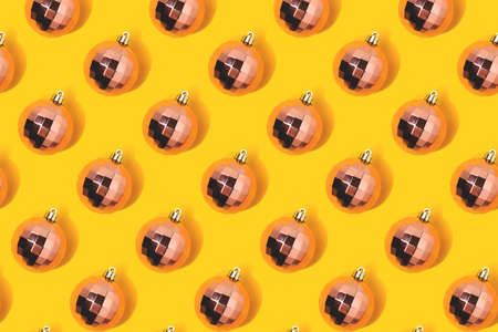 Repetitive pattern made from rose gold colored Christmas baubles on a yellow background.