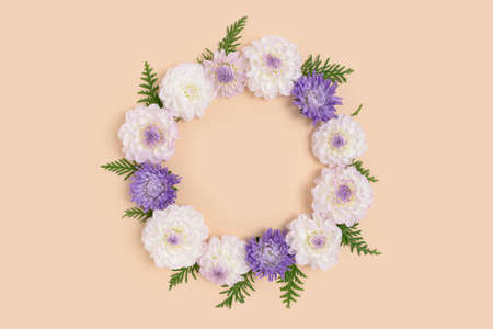 Wreath made of dahlia and green leaves on a beige background. Flower round frame with copyspace. Nature composition.の写真素材
