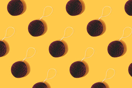 Repetitive pattern made of red paper Christmas baubles on a yellow background.