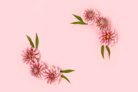 Flower border frame made of dahlia and green leaves on a pink pastel background. Springtime holidays...