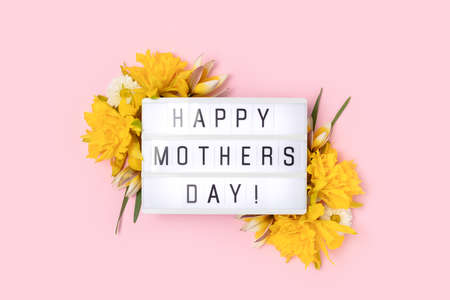 Happy Mothers Day. Lightbox with quote and frame made of yellow narcissus on a pink pastel background.の写真素材