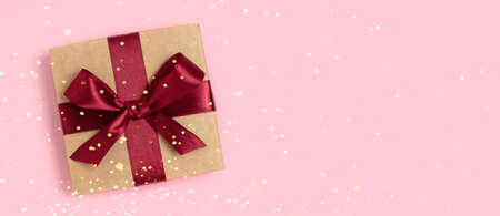 Banner with gift box tied with red ribbon on a pink background. Christmas concept with shiny golden bokeh.の写真素材