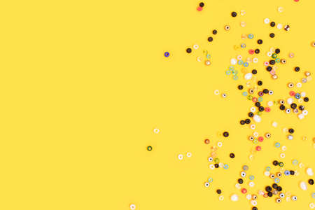 Multicolored beads scattered on a yellow background with copyspace.