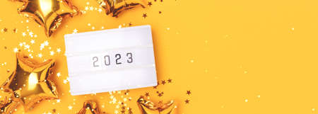 Banner with lightbox with 2023 numbers on a yellow background with place for text. Golden confetti and stars foil balloons.の写真素材