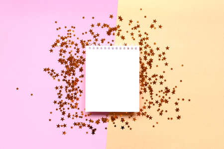 Blank notepad mockup with shiny stars confetti on a pink and gold colored background.
