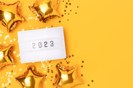 Lightbox with 2023 numbers on a yellow background with copy space. Golden confetti and stars foil balloons.の写真素材