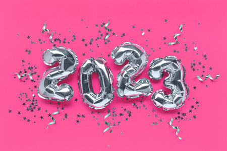 2023 silver foil balloons, stars confetti and ribbons on a pink background. Festive concept.