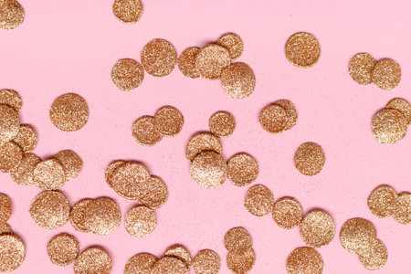 Round glittering gold confetti scattered on a pink background. Creative festive backdrop.