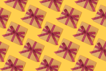 Repetitive pattern made from gift boxes with red ribbons. Creative concept on a yellow background.の写真素材