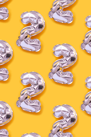 Repetitive pattern made of number two silver balloons. Creative concept on a bright yellow background.の写真素材