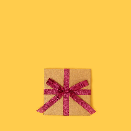 Gift box with red ribbon. Creative concept on a yellow background.