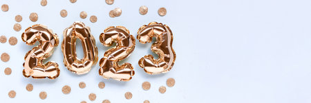 Banner with 2023 golden foil inflatable balloons and round glittering confetti on a blue background....