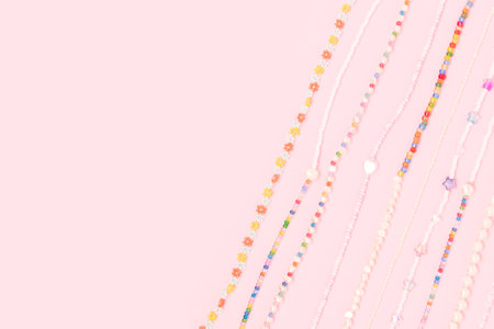 Necklaces made from colorful beads and pearls on a pink background with place for text.