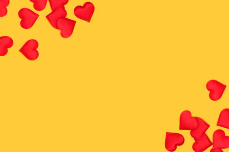 Frame made of red textile hearts confetti scattered on a yellow background. Place for text.