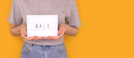 Banner with word sale. Woman hold in hands lightbox with letters in front of yellow background. Place for text.の写真素材