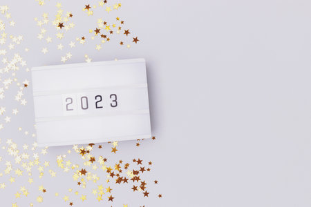Lightbox with 2023 numbers on a blue pastel background with golden stars confetti. Place for text.