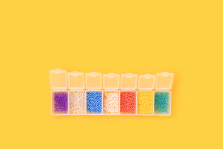 Multicolored beads in a transparent storage container on a yellow background.の写真素材