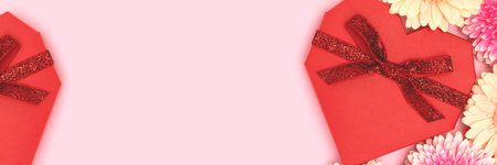 Banner with red gift box in a heart shape and gerbera flowers on a pink pastel background. Festive composition withcopy space.の写真素材