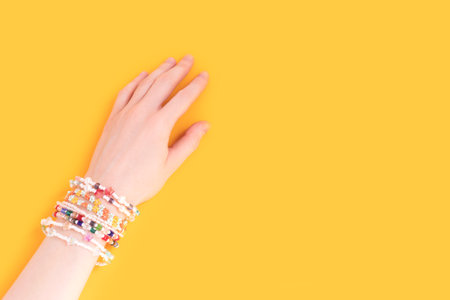 Female hand with a lot of bracelets on it. Trendy handmade jewelry made of pearls and beads on a yellow background.の写真素材