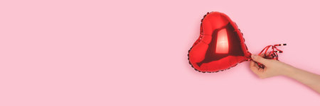 Banner with female hand hold red inflatable foil balloon in a heart shape.の写真素材