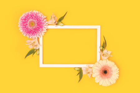 Frame made of green leaves, alstroemeria and gerbera flowers on a yellow background.の写真素材