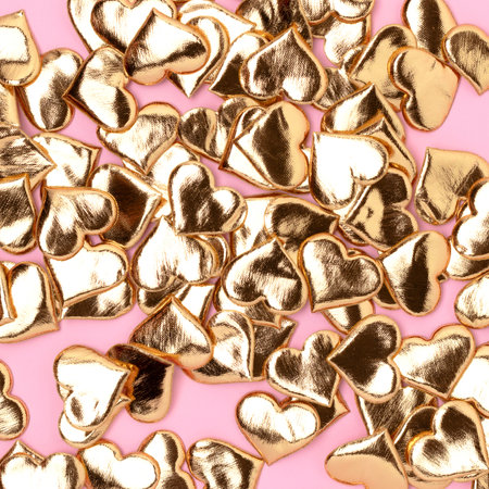 Texture made of gold colored hearts confetti on a pink background.の写真素材