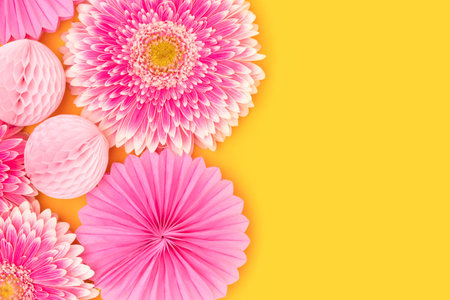 Pink gerbera flowers, tissue paper fans and balls on a yellow background. Place for your design.の写真素材