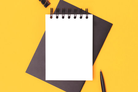 Workspace with clean notepad mock up and black colored stationery on a yellow background. Business...