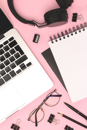 Layout with laptop, headphones, eyeglasses and black colored stationery on a pink background. Online...