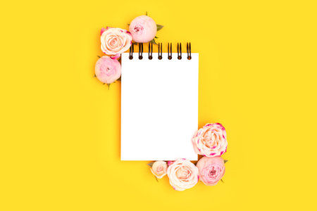 Empty notepad mockup. Pink rose flowers on a yellow background. Festive floral concept.の写真素材