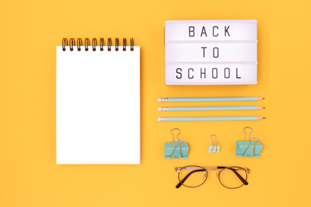 Back to school. Lightbox with letters and mint colored stationery on a yellow background. Clean notepad mockup.の写真素材